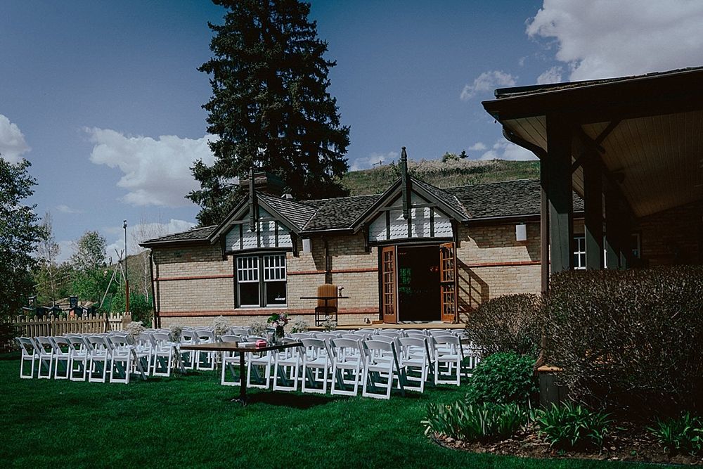 White chairs set up for outdoor wedding ceremony in front of Tudor-style building.