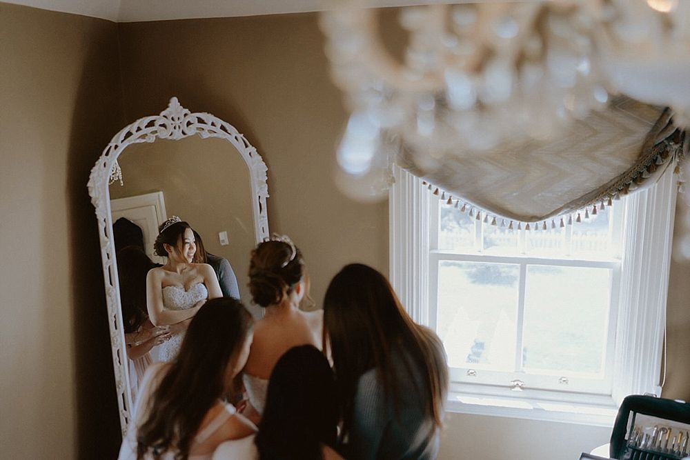 Wedding preparation scene reflected in ornate vintage mirror with window light.