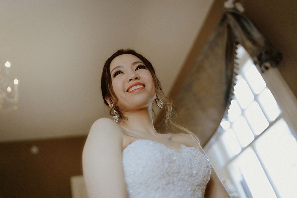 Radiant bride in a strapless lace wedding gown standing by a bright window.