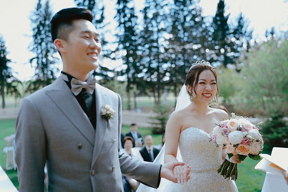 Wedding ceremony outdoors with evergreen trees and soft spring light.