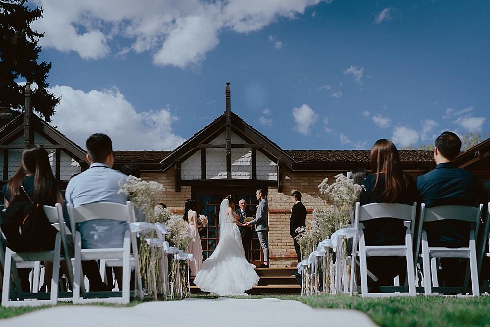 Wedding venue setup with white chairs and a Tudor-style building backdrop on a sunny day.