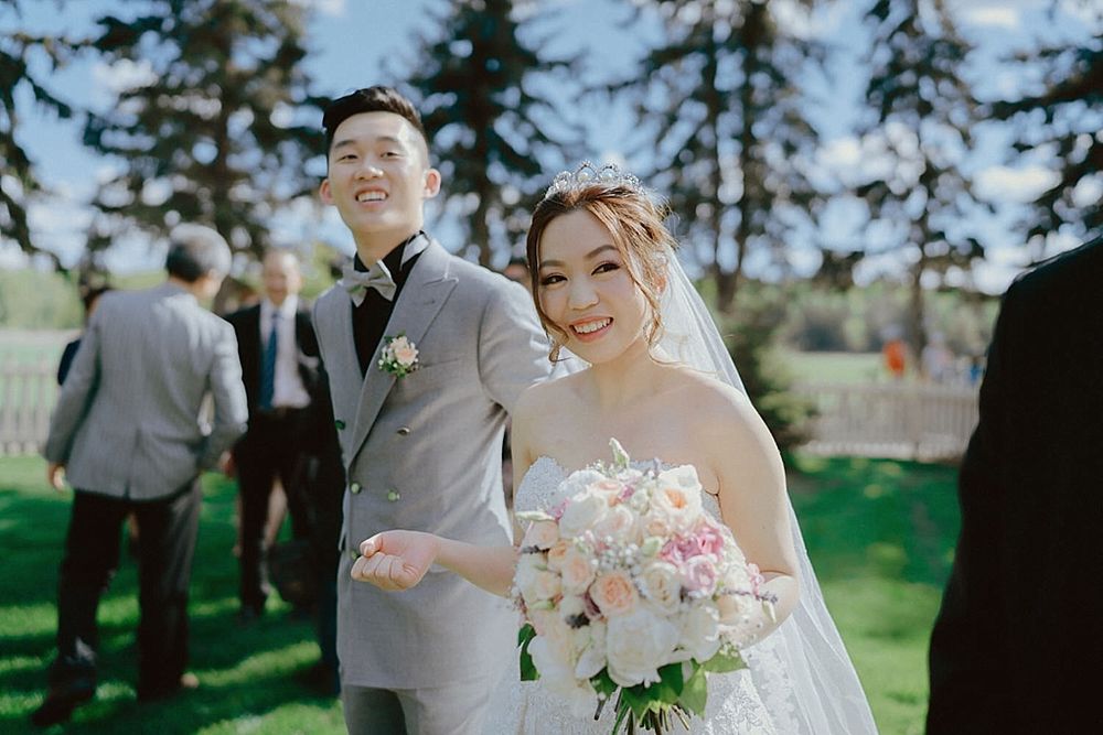 A joyful wedding celebration outdoors on a sunny day with evergreen trees in the background.