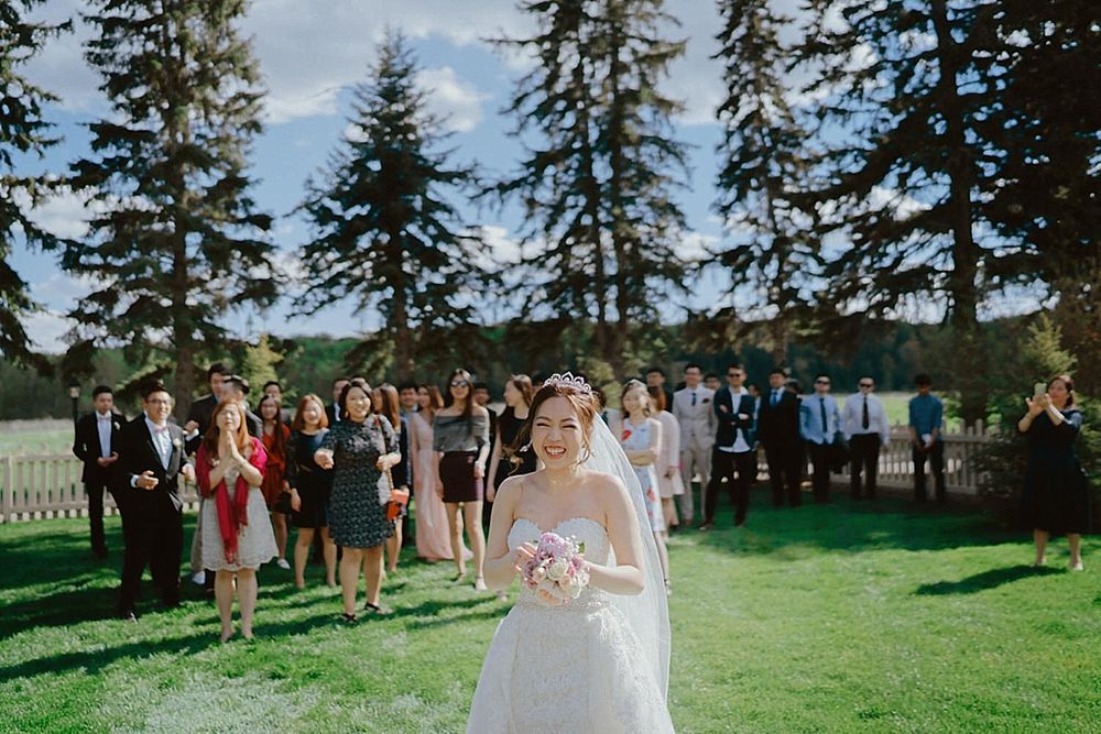 Wedding guests gather on a manicured lawn with evergreen trees creating a natural backdrop.