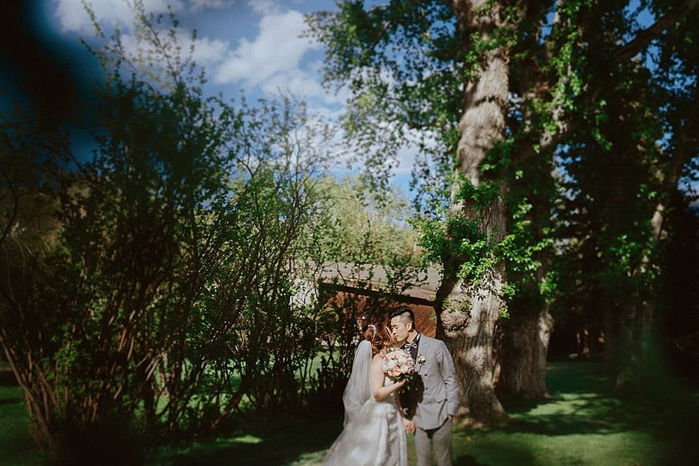 A romantic outdoor wedding portrait with sunlight filtering through trees and vibrant greenery.