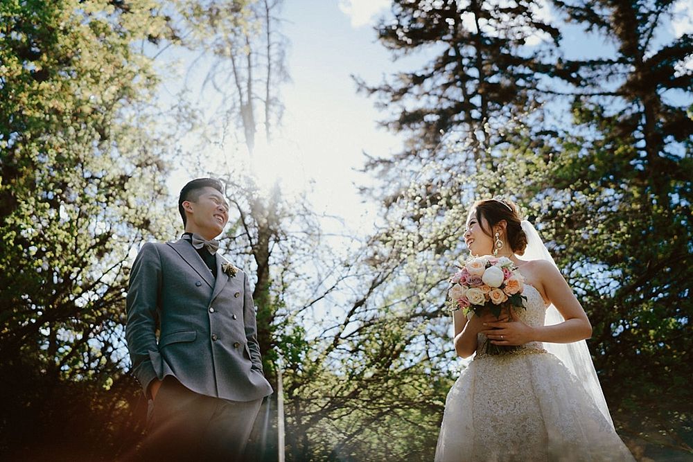 A couple shares an intimate moment during their wedding photoshoot in a sunlit wooded area.