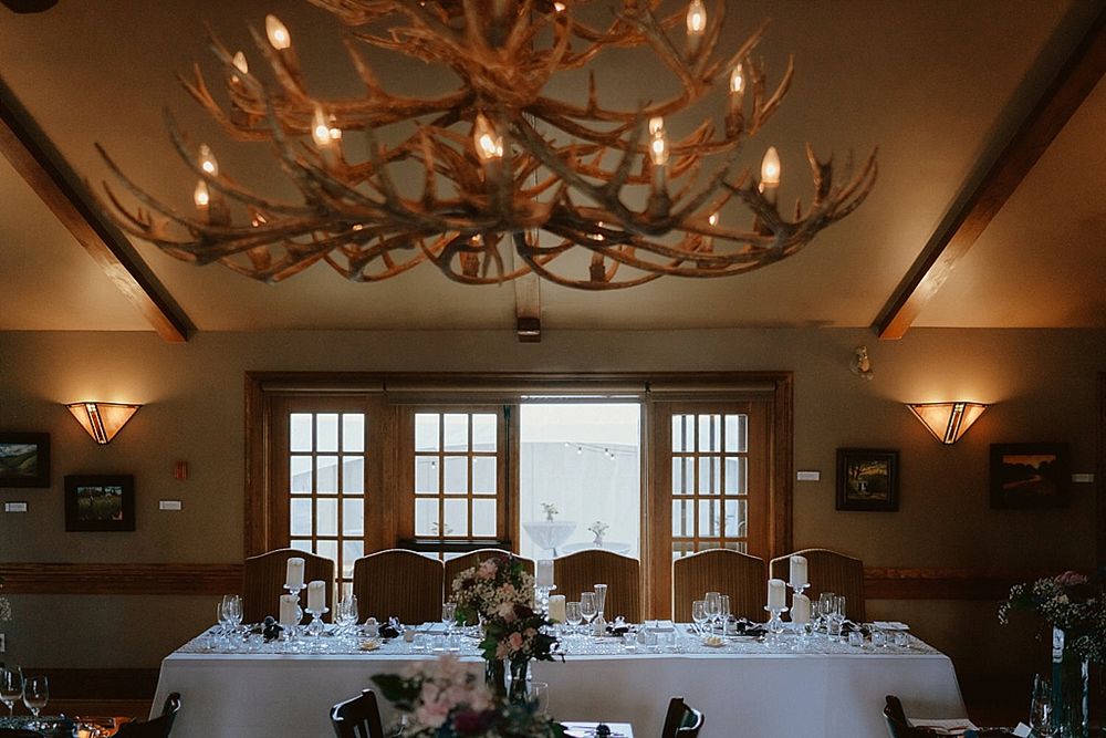 Elegant dining room with antler chandelier and French doors overlooking mountain view features white-clothed tables for reception.