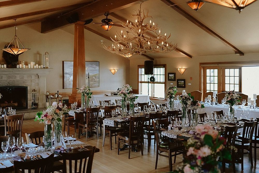 Elegant wedding reception venue with rustic wood beams, chandeliers, and tables decorated with soft pink floral centerpieces.