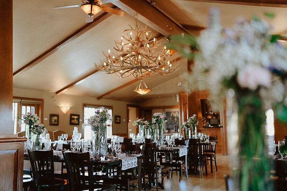 Wedding reception venue interior with exposed wood beams, rustic decor, and floral arrangements on tables.