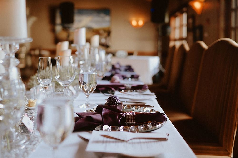 An elegant table setting with burgundy napkins and wine glasses glows warmly in a romantic restaurant interior.