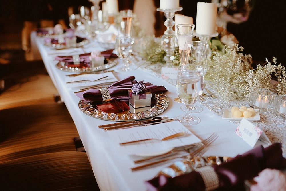 Elegant wedding reception table setting with white linens, candles, and baby's breath floral arrangements at dusk.