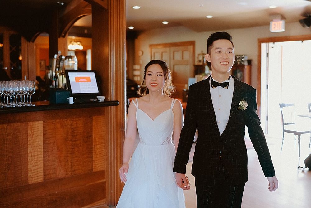 Couple walking together through an elegant reception venue with a bar counter visible in the background.