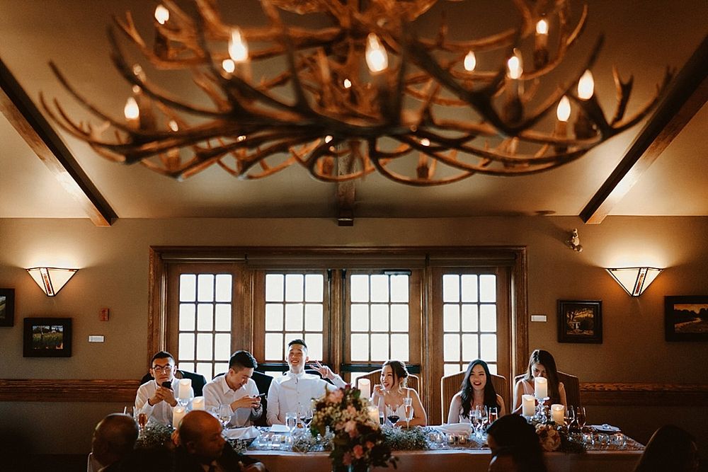 Wedding reception room with antler chandelier and guests seated at decorated tables.