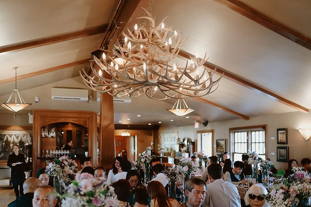 Elegant wedding venue with antler chandelier and floral centerpieces on tables.
