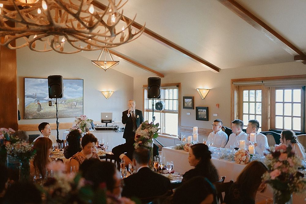 Wedding reception venue with guests seated under antler chandelier and wall sconces.