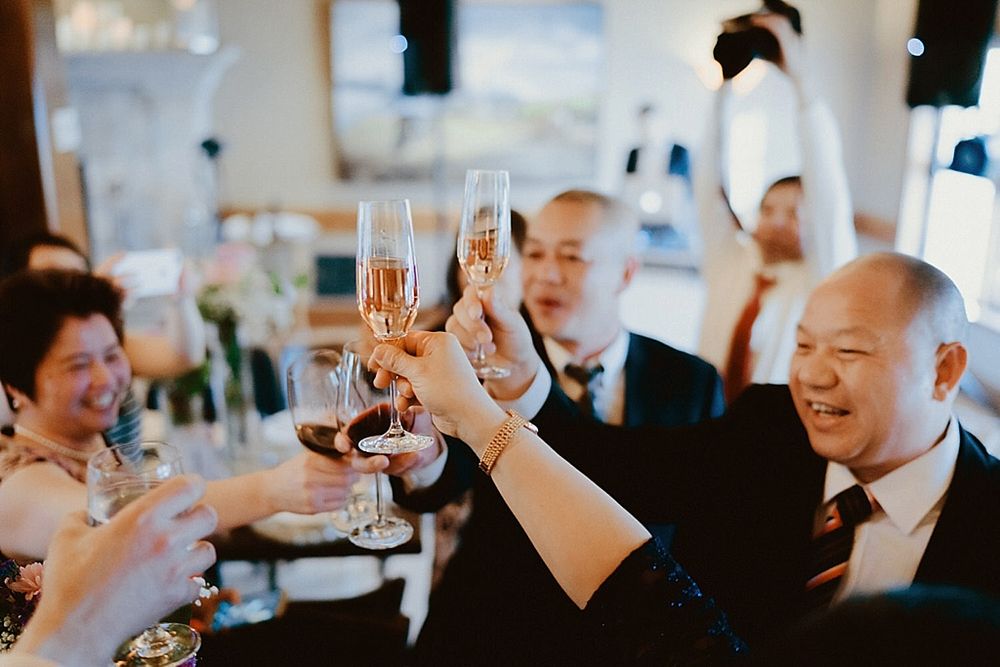 Wedding guests raise champagne glasses during a celebratory toast at an elegant indoor reception.