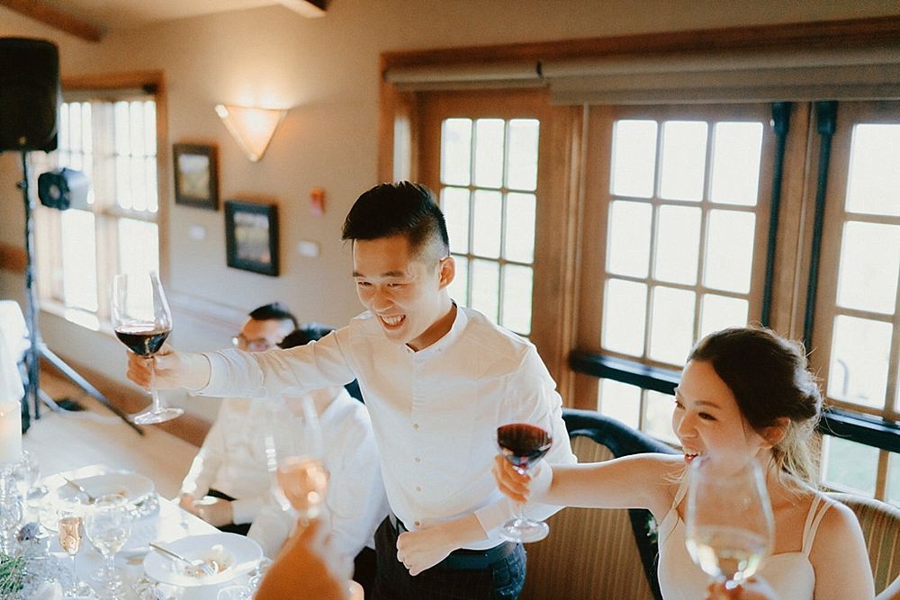 Guests raise wine glasses during a toast at an elegant indoor wedding celebration.