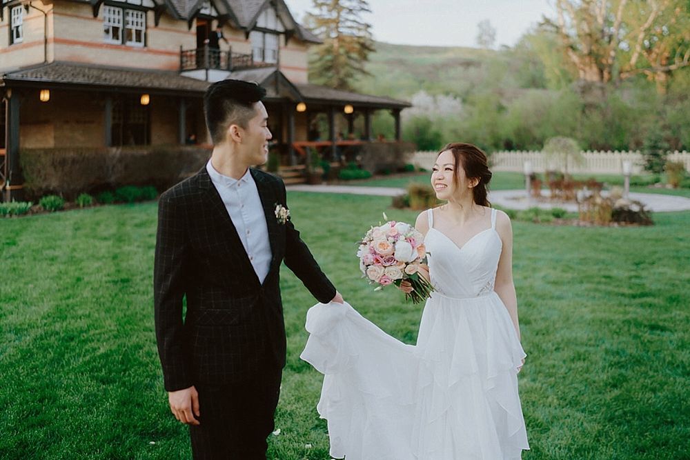 A bride and groom share a tender moment while walking through a green countryside setting at sunset.