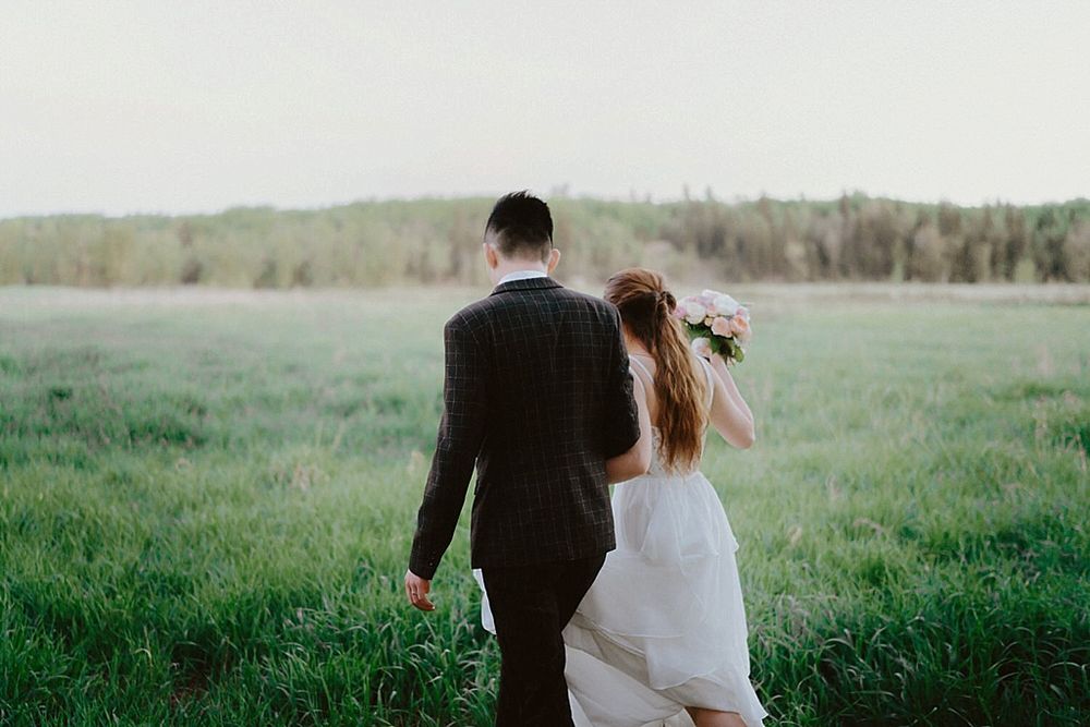 A newlywed couple walks hand in hand through a scenic outdoor path surrounded by spring greenery.