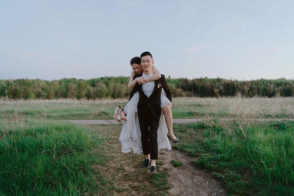 Newlyweds walk together through a rustic outdoor setting with natural grassland scenery.