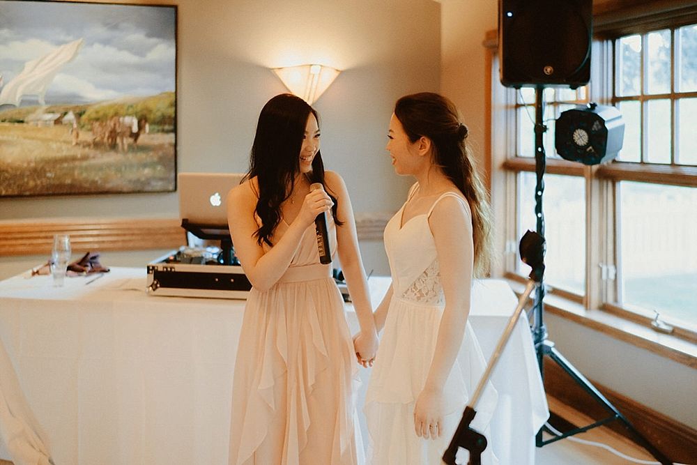 Two attendees share a tender moment at a wedding reception with decorative lighting and rustic decor.