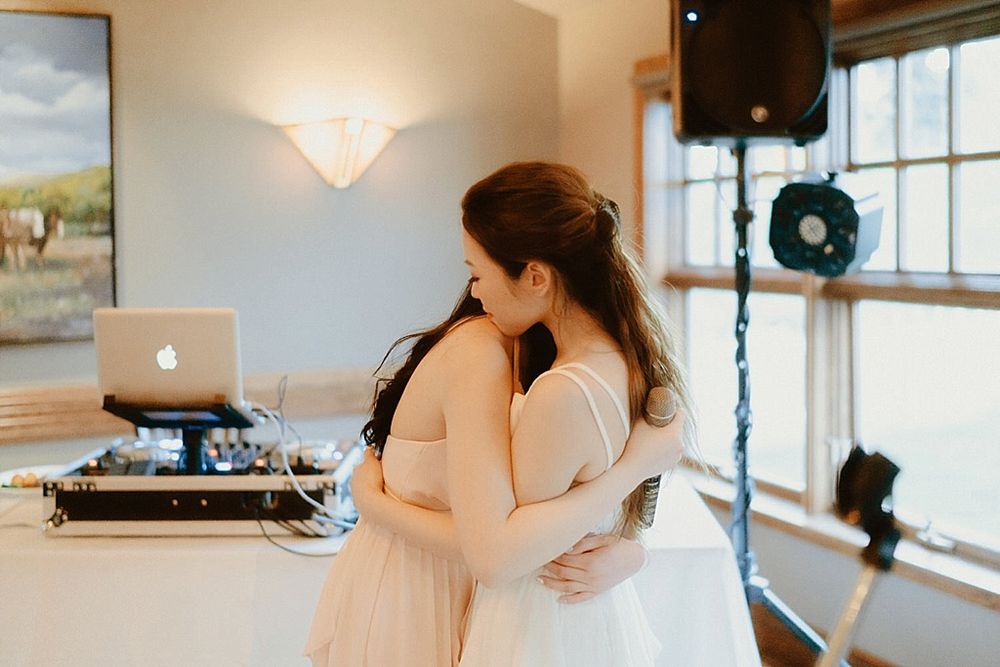 Two people embrace in an elegant reception venue with a pastoral painting and turntables visible.