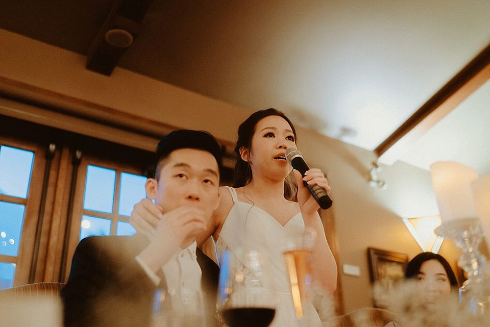Reception guests listen attentively during speeches in a warmly lit dining room.
