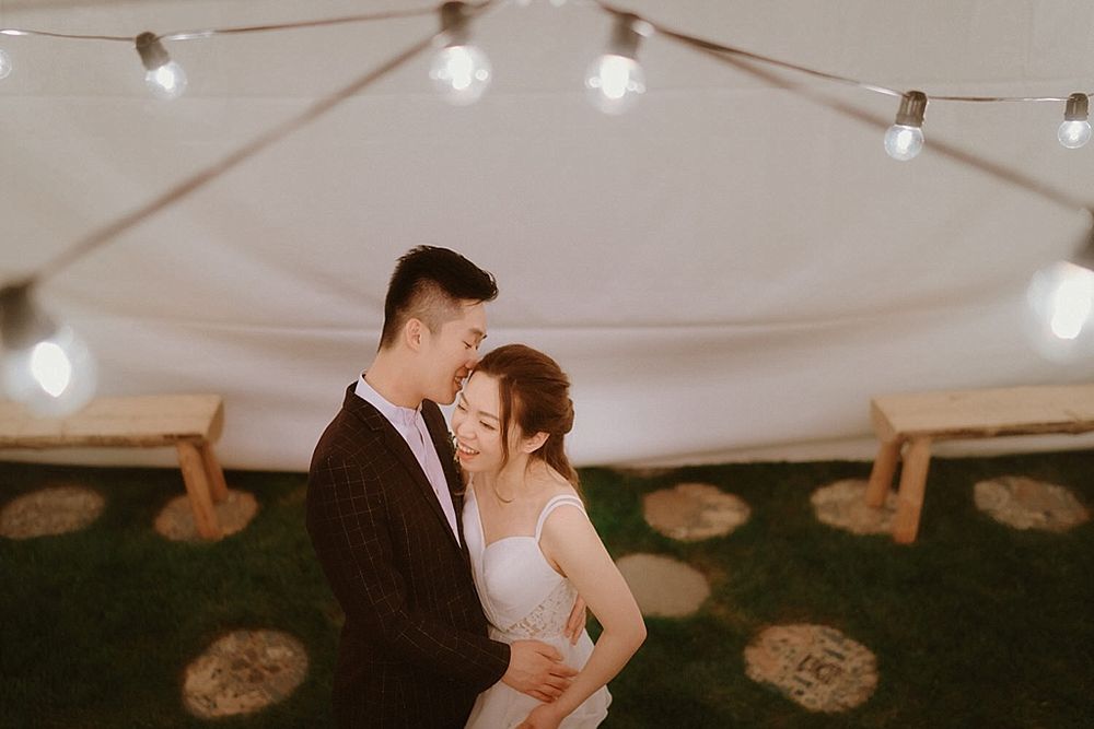 String lights hang overhead at an outdoor wedding reception under a white tent.