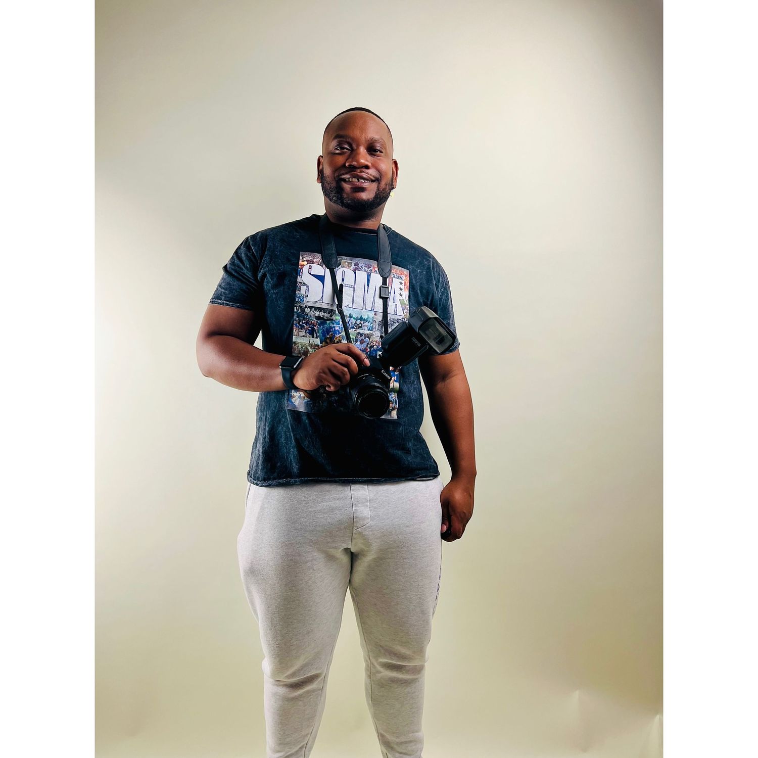 A person in a black graphic t-shirt and white pants poses confidently against a light background.