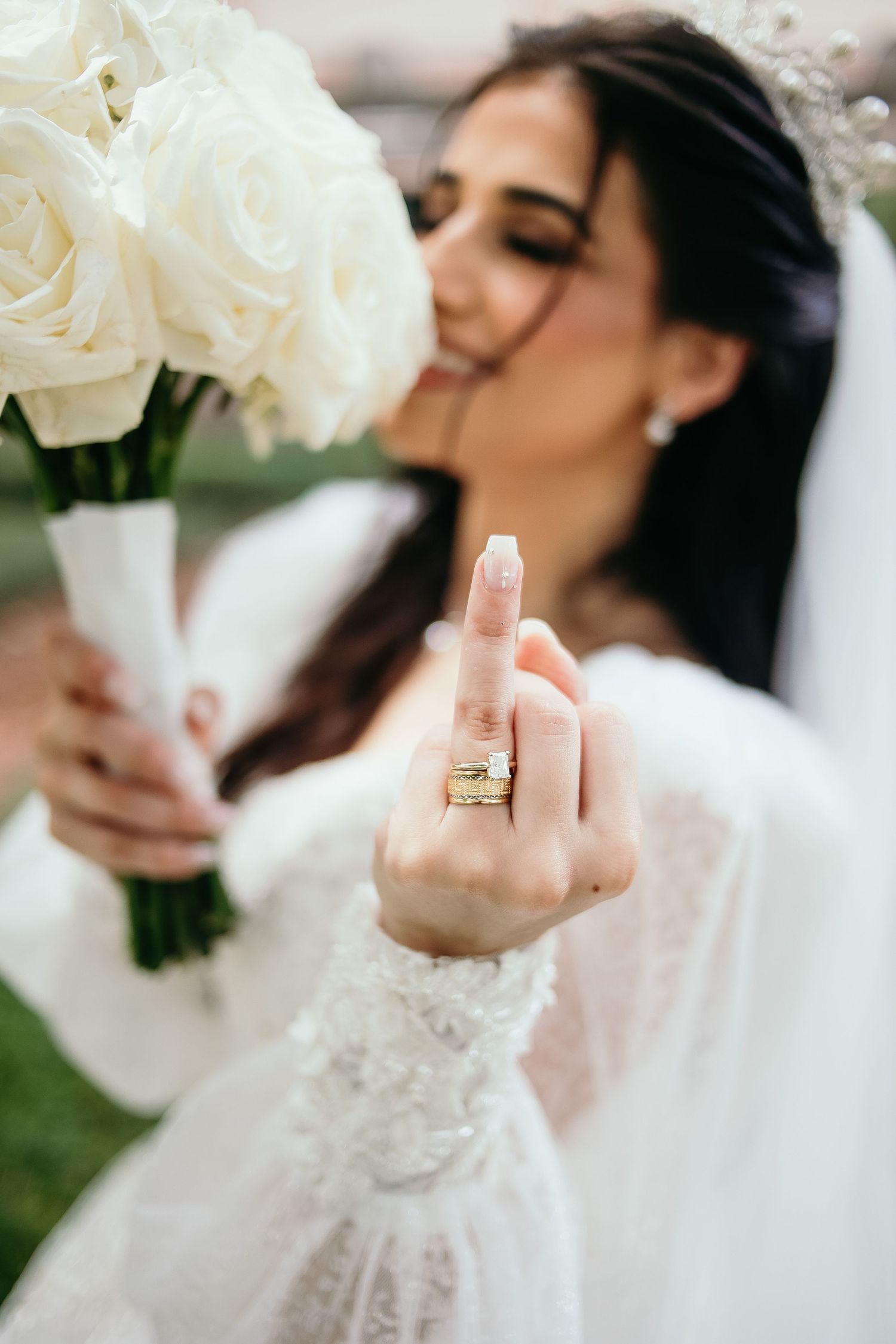 Wedding detail shot showing white bouquet and bridal gown lace sleeve with engagement ring.