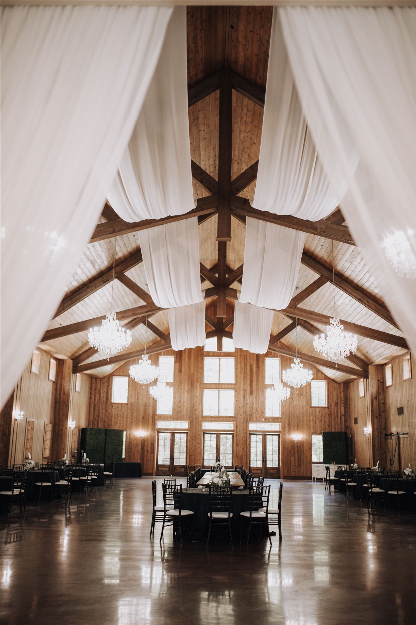 Elegant reception hall with white draped ceiling, wooden beams, and crystal chandeliers.
