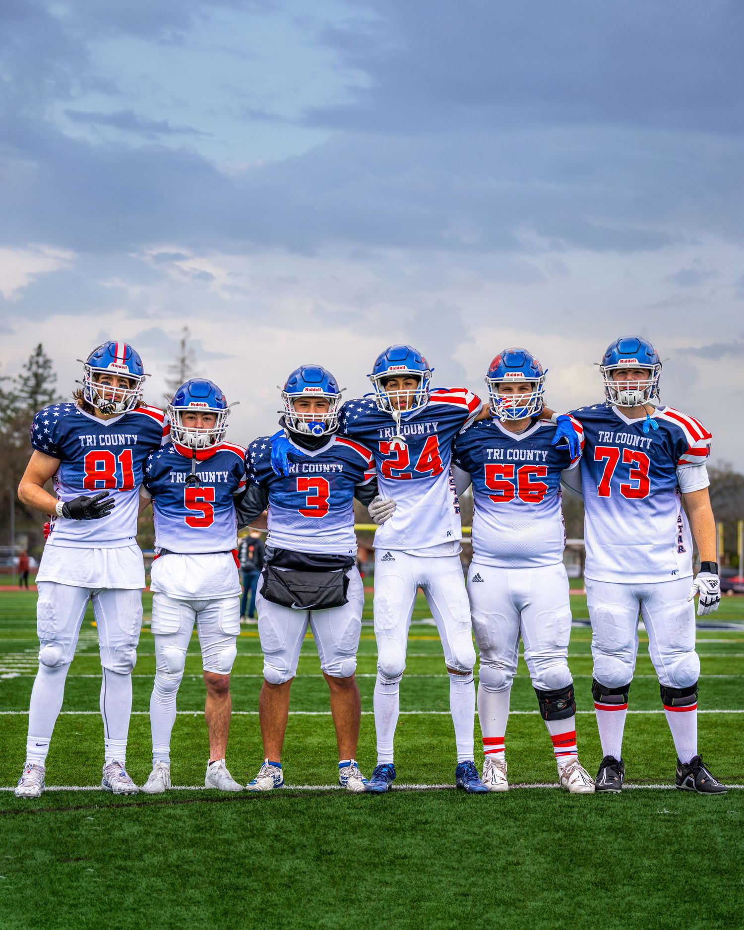 High school football team in blue and white uniforms poses together on field at sunset.