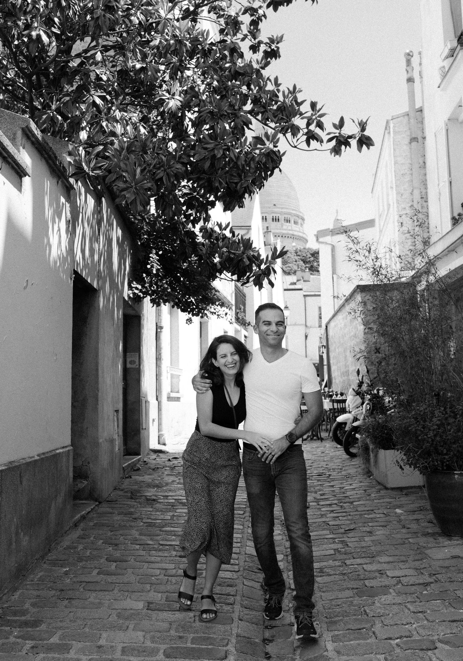 A couple posing on a charming cobblestone street with Montmartre's Sacré-Cœur visible in background.
