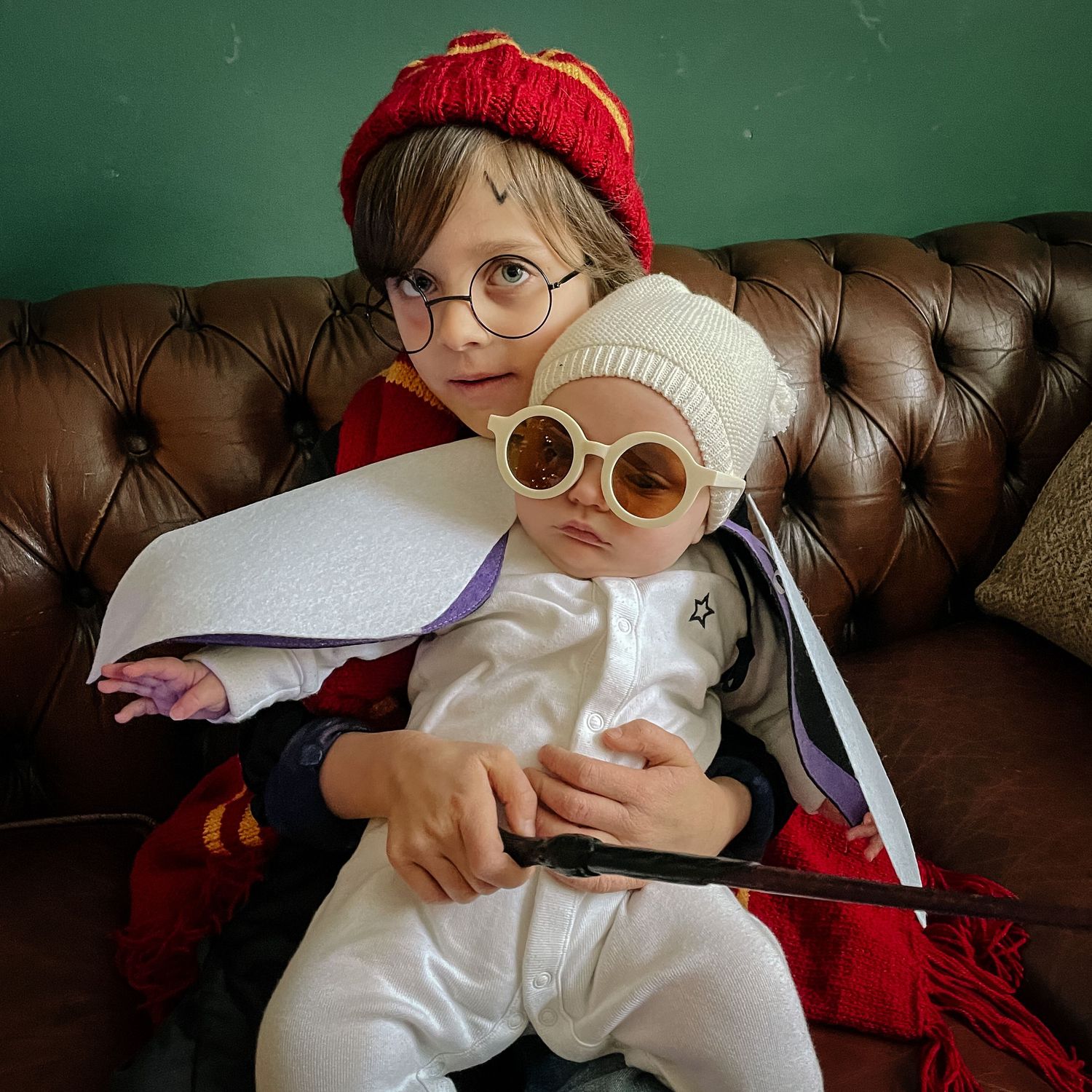 Whimsical portrait of children in winter accessories sitting on leather couch.