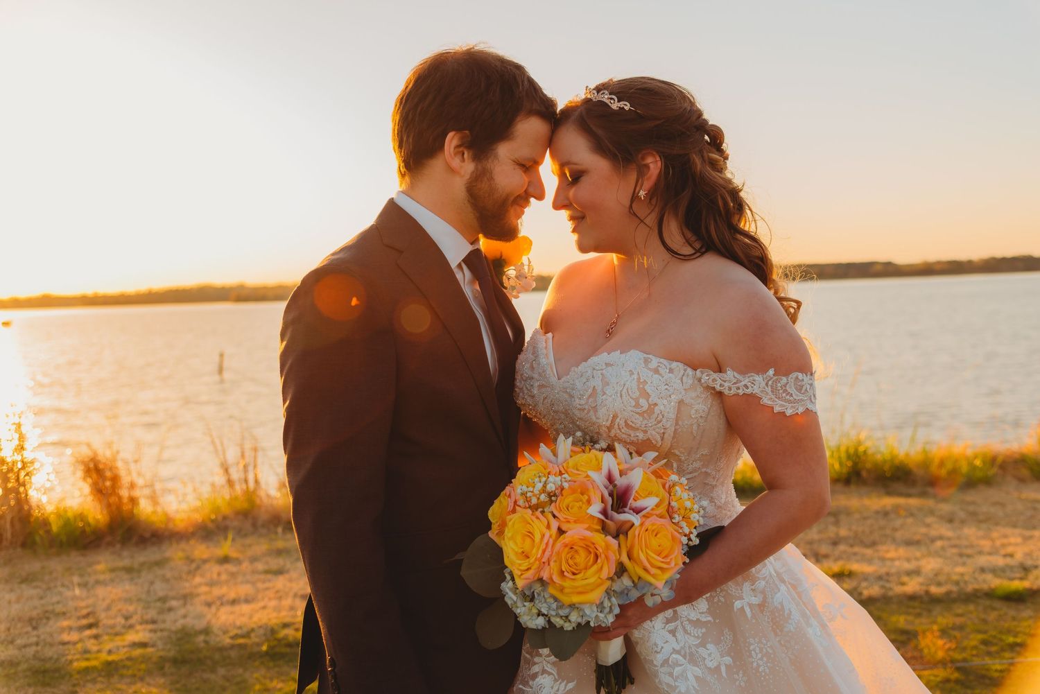 A sunset wedding portrait with a golden glow and yellow bouquet by the water.