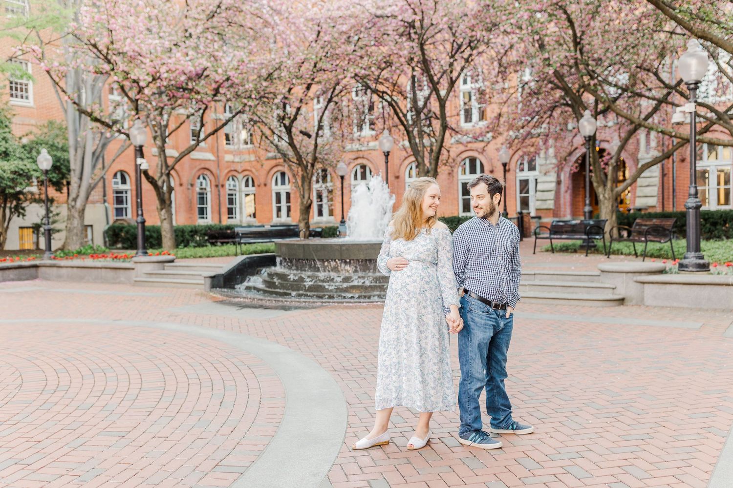 A couple walks together on a brick pathway surrounded by blooming cherry trees.