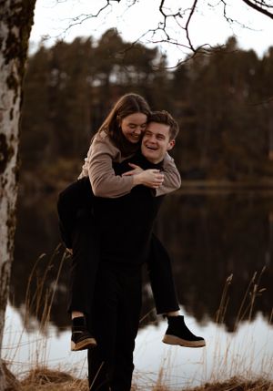 Playful piggyback moment captured beside a calm lake with trees silhouetted in the background.