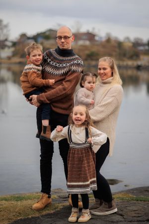A family wearing coordinated knit sweaters poses together by a lake.