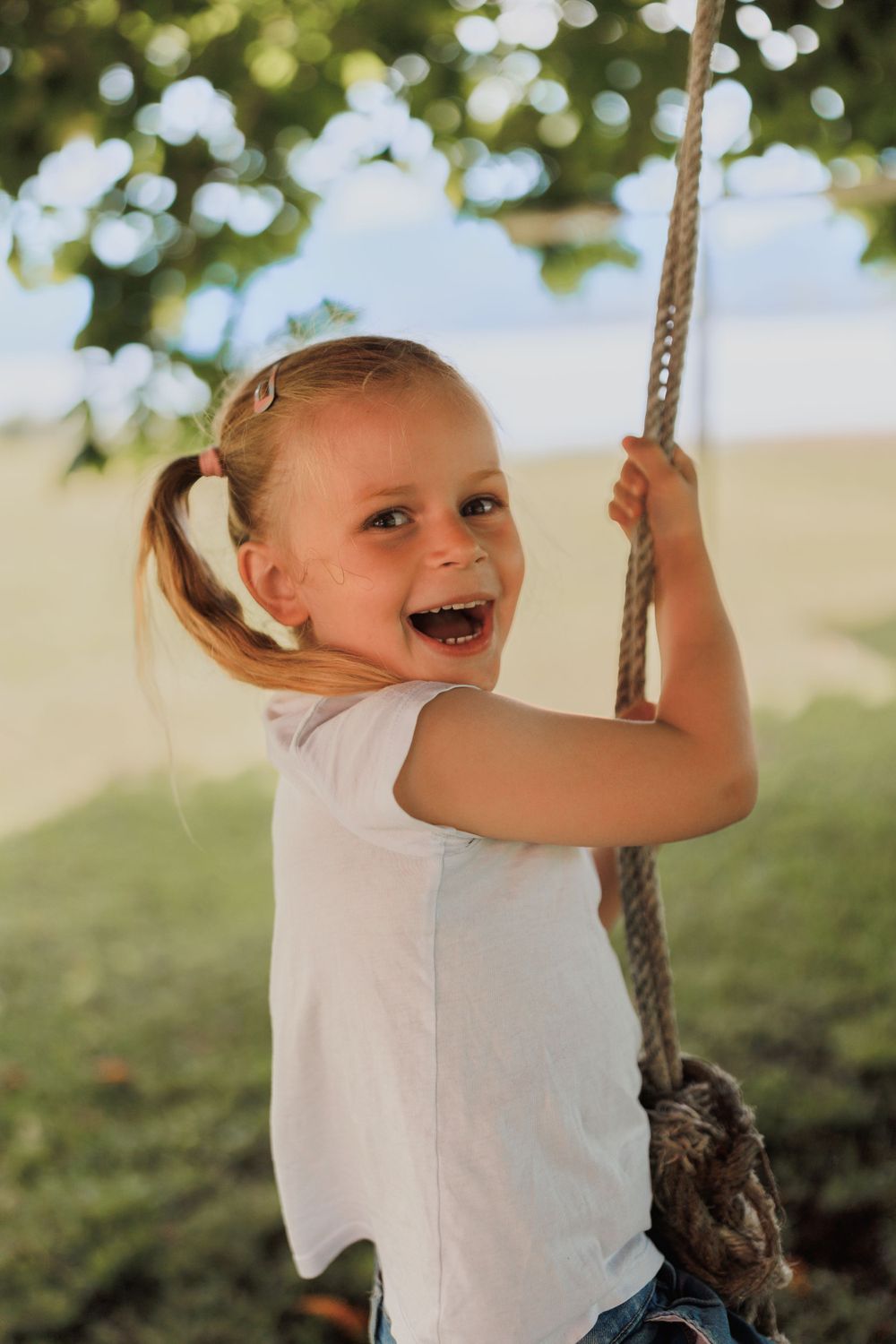 A joyful child swinging on a rope swing outdoors with a bright smile and ponytail.