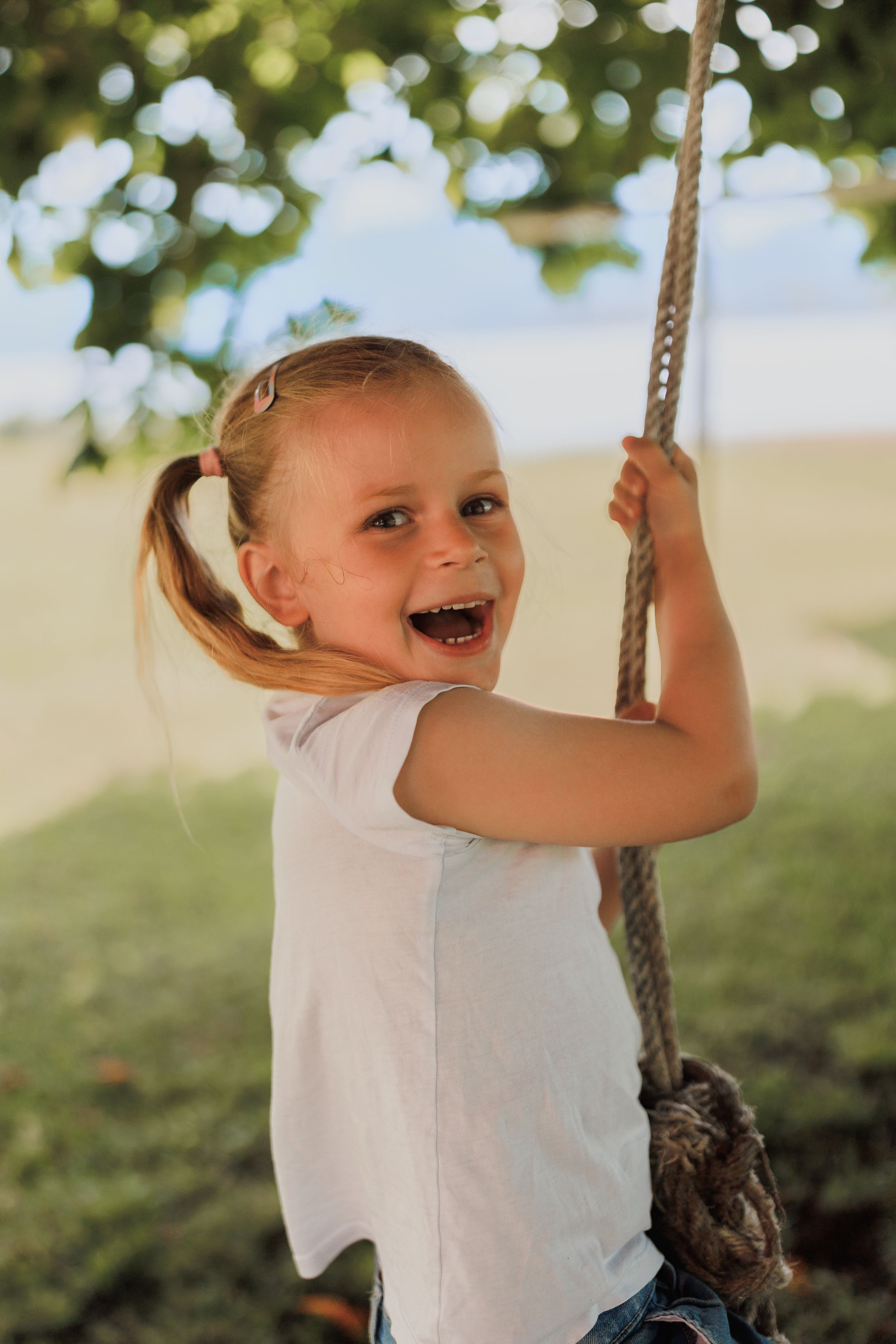 A joyful child swinging on a rope swing outdoors with a bright smile and ponytail.