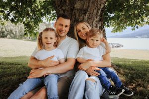 A family of four sitting together under a tree near a lake on a sunny day.