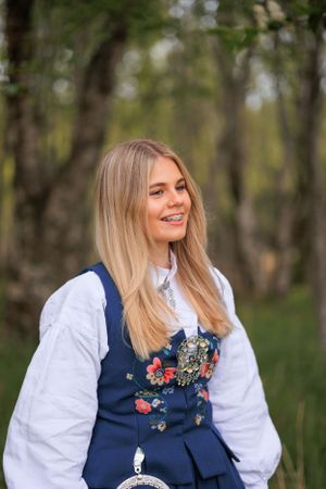 A blue embroidered folk dress with floral details and traditional silver jewelry worn in a natural outdoor setting.