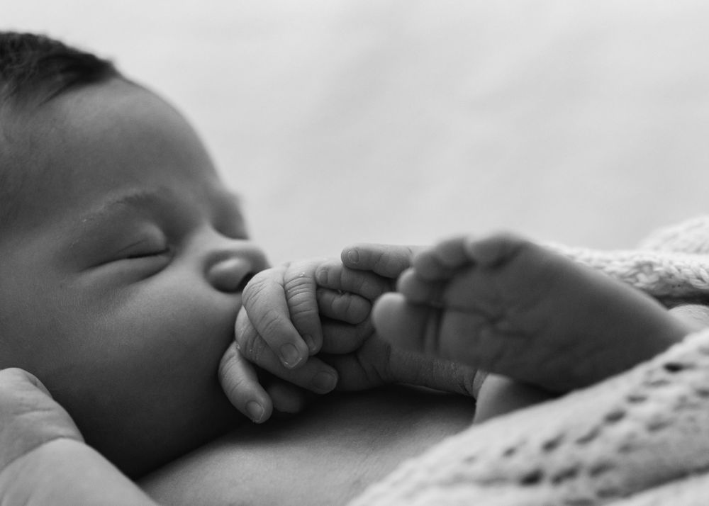 Close-up black and white image of sleeping infant's face and tiny hand.