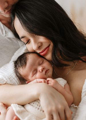 Tender moment between parent and sleeping newborn on white blanket.