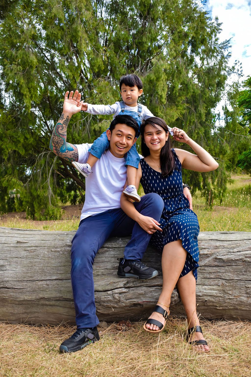 Happy family sitting on fallen log in forest park waving at camera.