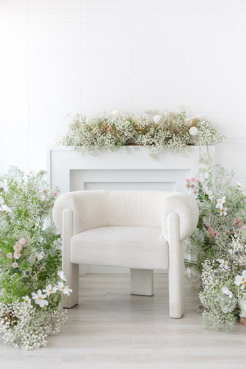 White armchair surrounded by fresh baby's breath and floral arrangements in a light-filled room.