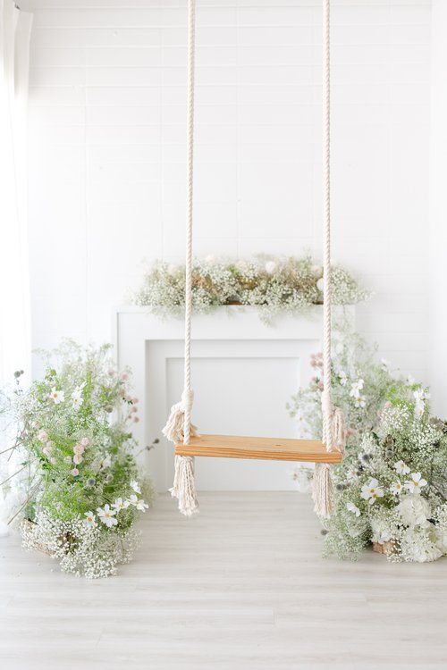 White wooden swing decorated with baby's breath and greenery in a bright minimalist setting.