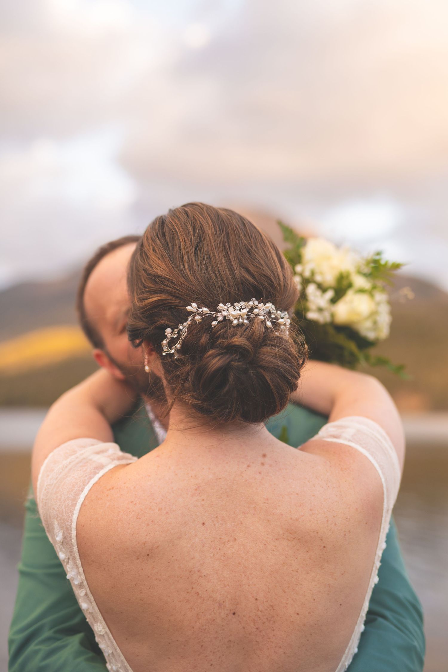 back of a bride's head with her arms wrapped around her groom holding bouquet