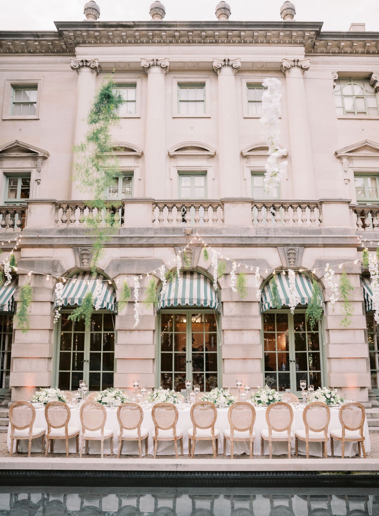 Elegant pink stone building with striped awnings and row of decorated chairs for outdoor event.