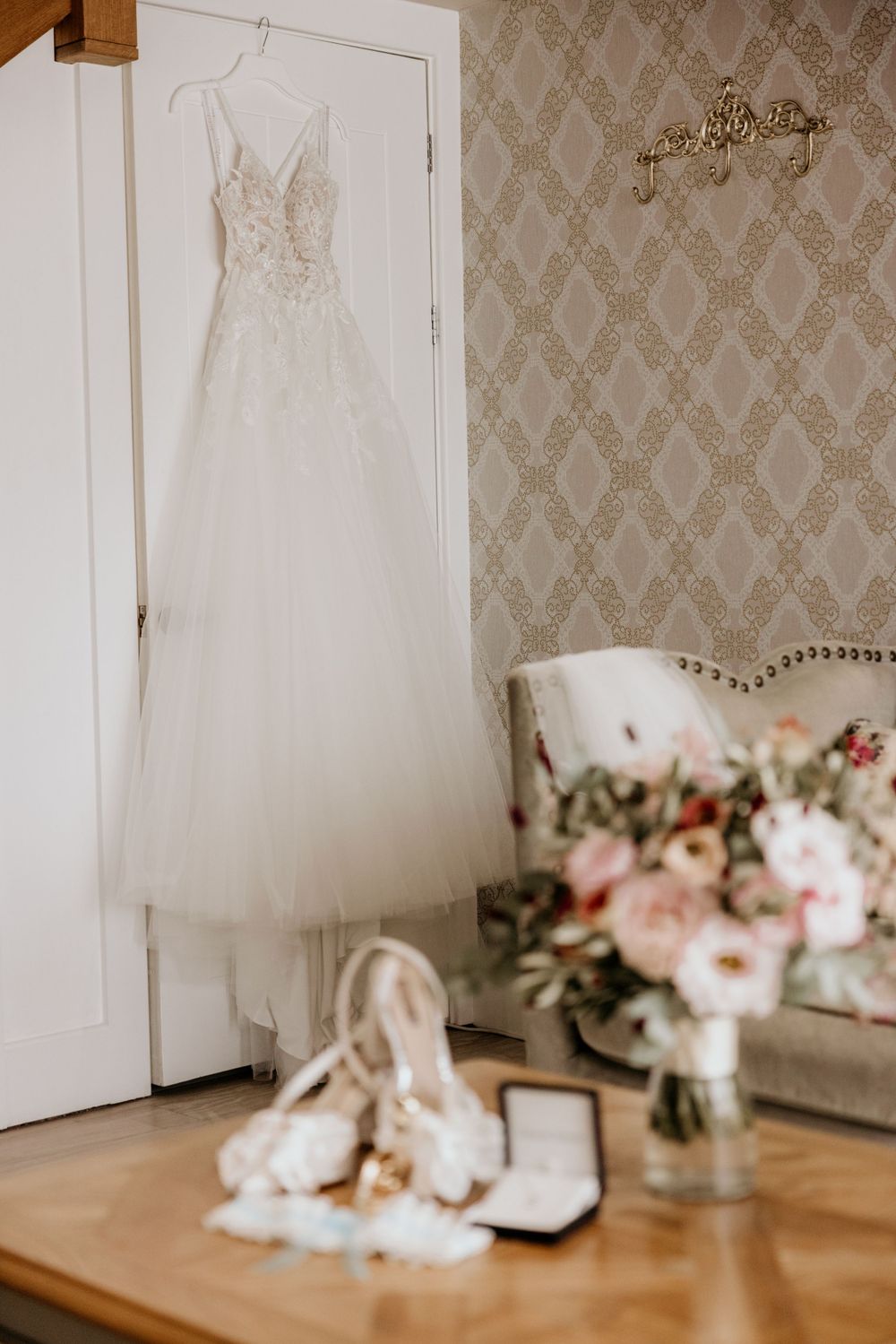 Elegant white wedding dress hanging with floral bouquet and accessories below.