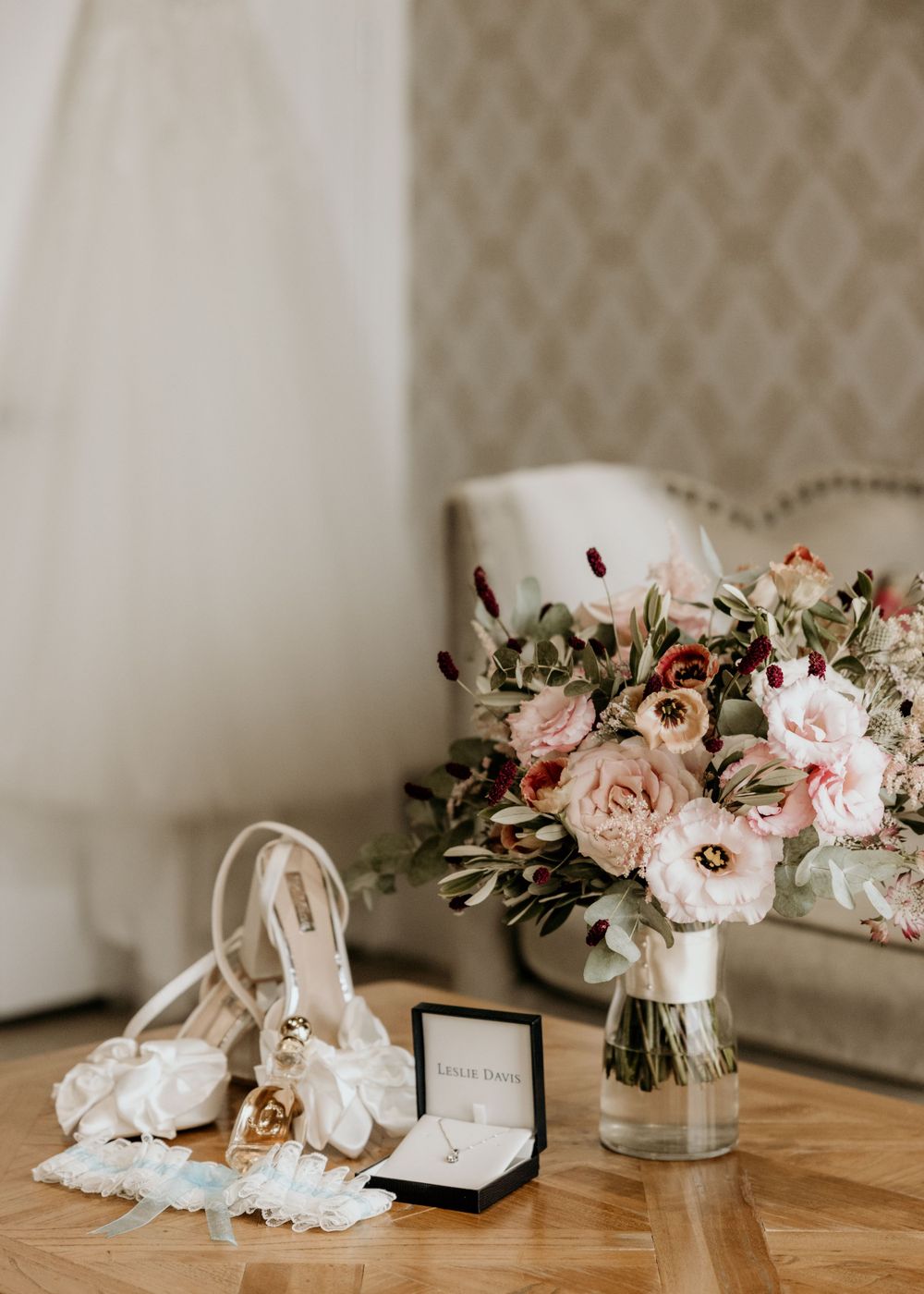 Wedding details including blush bouquet, jewelry box, and bridal accessories on wooden table.